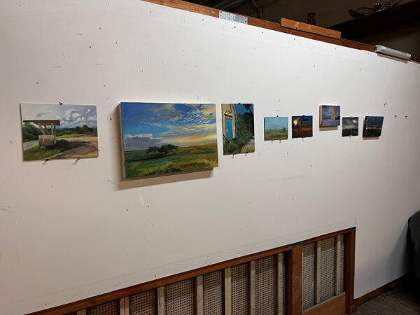 A photograph of a studio wall with several small landscape paintings by Elena Rodriguez.