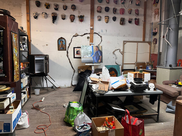 A photograph of an artist's studio with paintings and artist supplies around the space. 