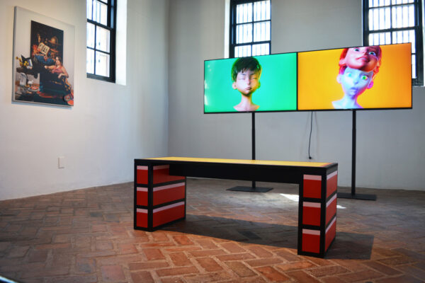 A cartoon-looking bench sits in the middle of the room. In front of the bench is a two-screen video, each screen featuring an animated character set against a colorful background.