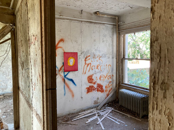 An abandoned building with graffiti on the walls. A painting hangs atop the graffiti.
