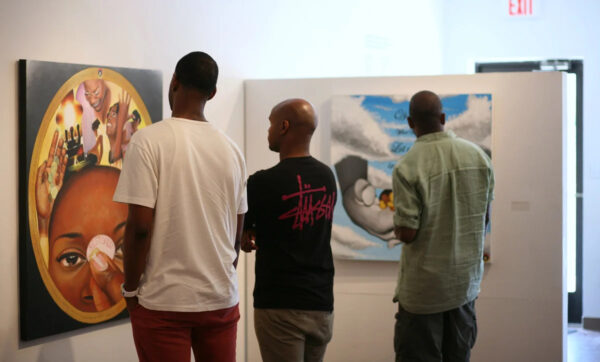 A photograph of three Black men looking at paintings by Sanah Brown in a gallery.