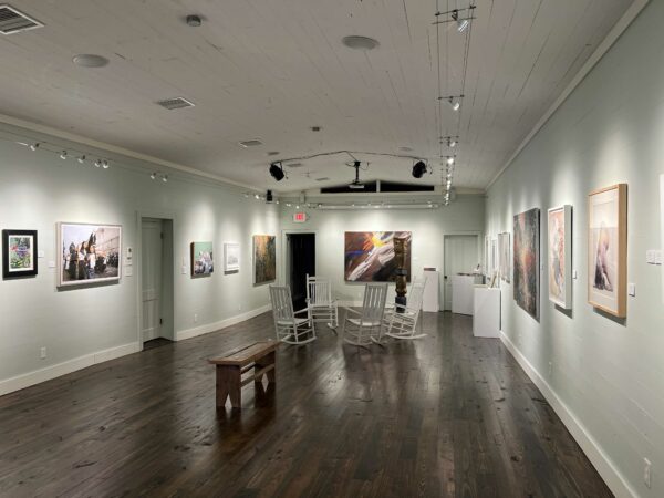A former theater room converted into a gallery with rocking chairs and a bench in the center and two dimensional works on the wall