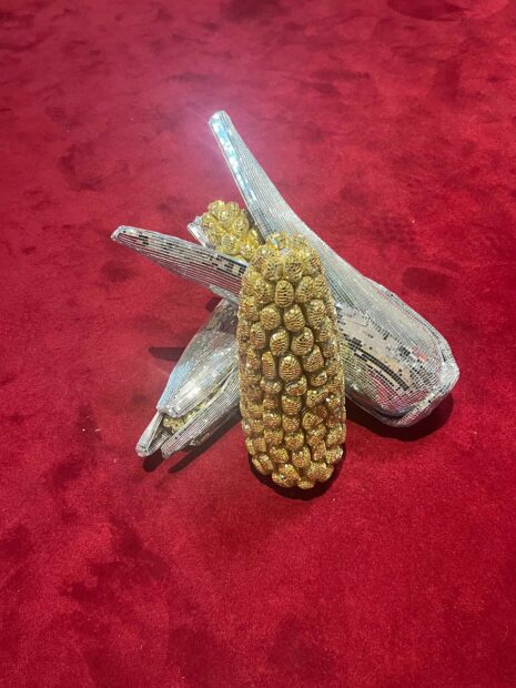A mirrored pinecone-looking object and other organic forms sit on a plush, red carpet.