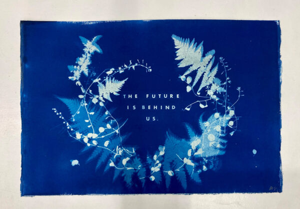 A blue cyanotype artwork featuring a wreath of leaves, in the center of which is the text "the future is behind us."