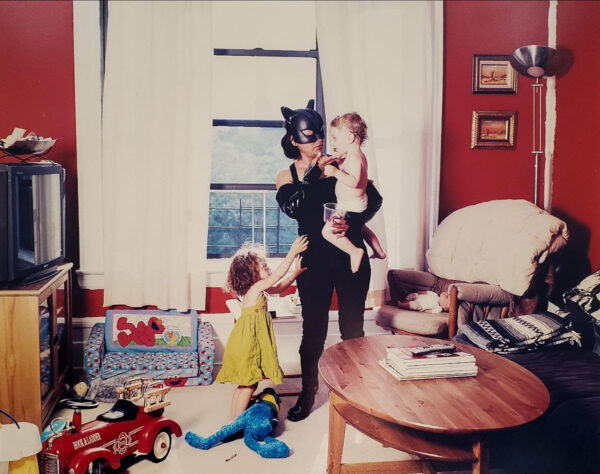 A photograph by Dulce Pinzón of a child caregiver wearing a batman costume while caring for two young children.