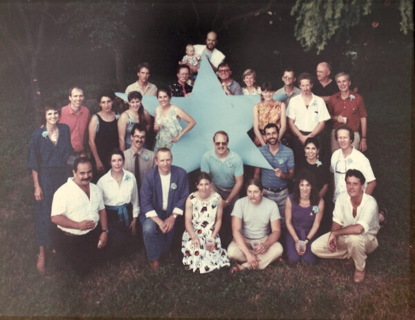 A photograph from 1986 of a group of artists gathered around a large blue star sculpture.