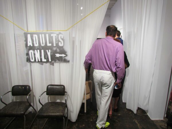 Installation view of an Adults Only sign hanging in front of a curtain
