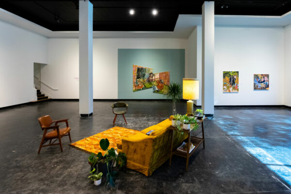 Installation view of paintings on a wall and a living room setup in a gallery