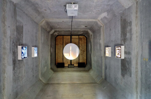 Installation view of a video projection and lightboxes in a cement tunnel