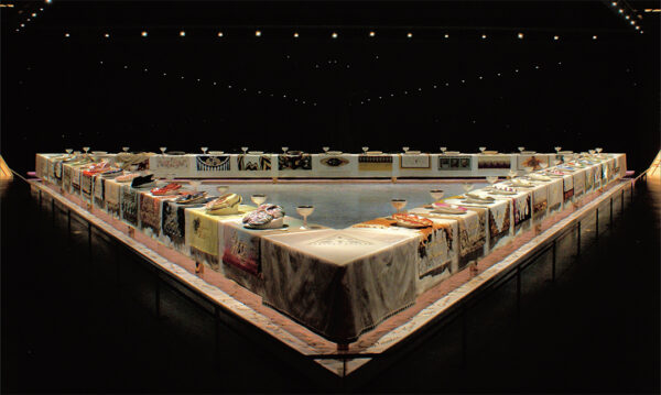 A photograph of Judy Chicago's "The Dinner Party," an extravagant triangle-shaped with 39 place settings. 