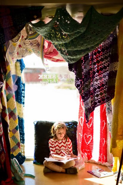Photo of a little girl drawing on the floor in a room surrounded by textiles