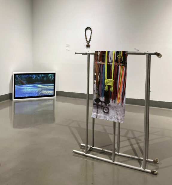 Installation view of a screen in a corner with a video of the artist sweeping and a photo hanging from a metal rod