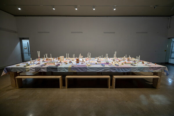A photograph of an installation by Sheryl Anaya, featuring a large rectangular table intricately set.