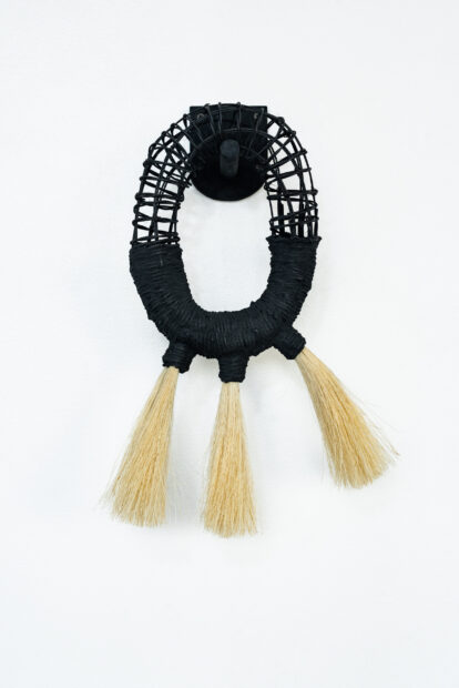 Round black basket sculpture hanging on wall with reed tassels