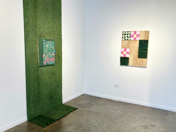 Installation view of two dimensional works on the wall, one hanging on top of astroturf