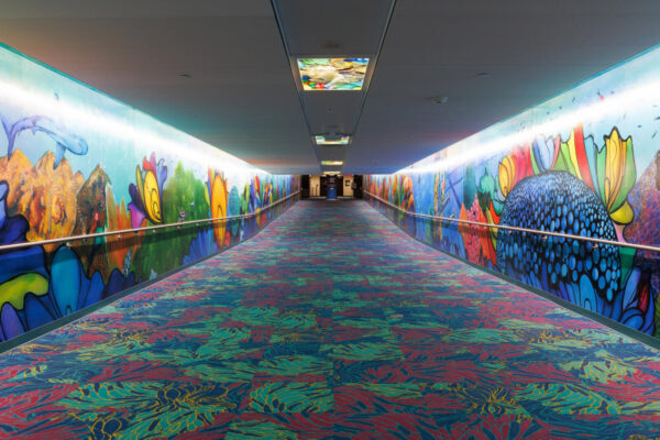A long pedestrian tunnel features a colorful carpet and wall paneling, making the pedestrian feel like they're underwater.