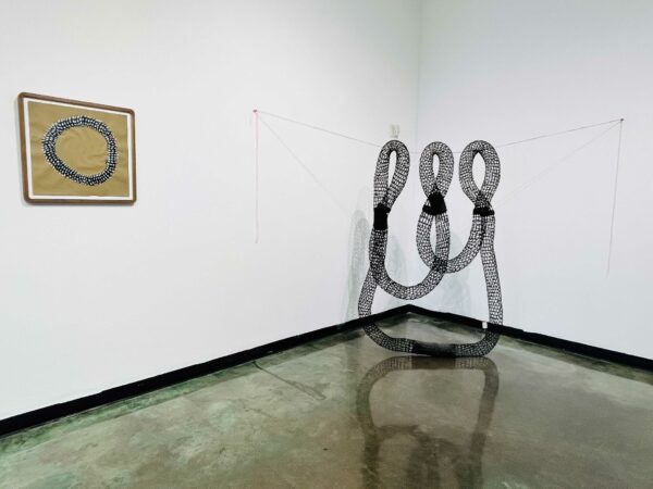 Installation view of a black basket sculpture suspended on a wire