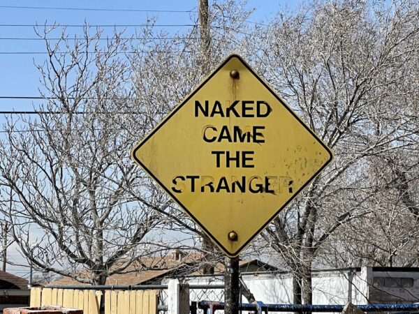 Yellow street sign with the text "Naked came the stranger"