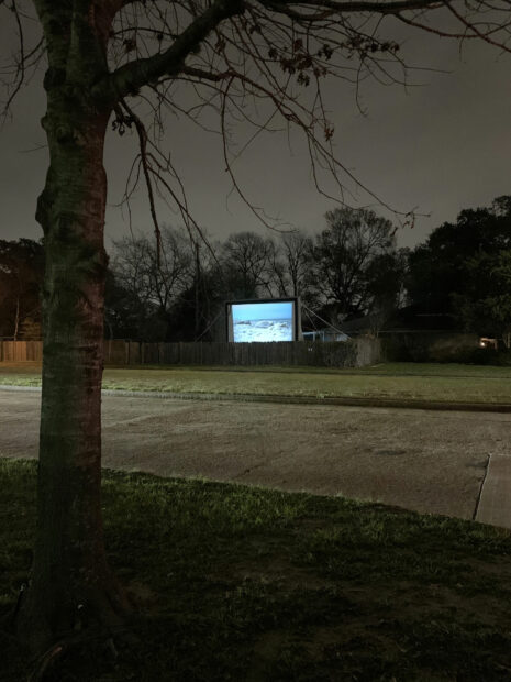 A large screen with movies projected onto it in a parking lot