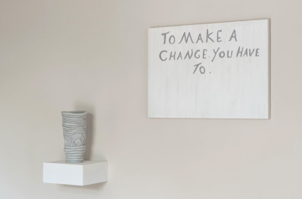 Ceramic vase on a floating shelf on the left and a small canvas saying "to make a change you have to " on the right