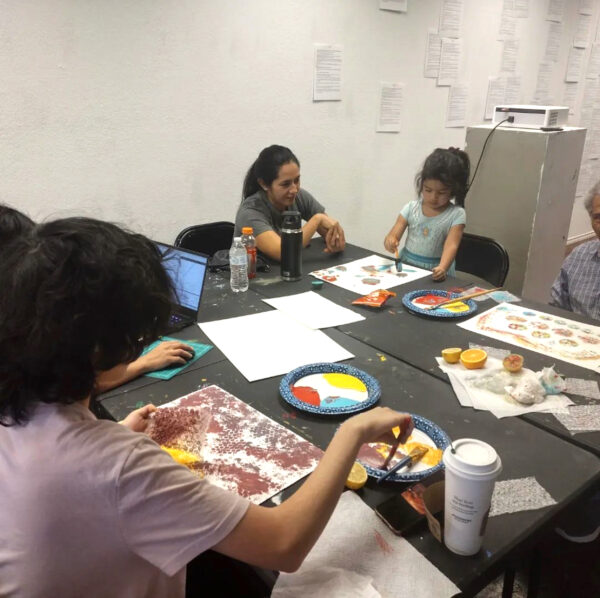 A photograph of a small group of people seated at a table and painting.
