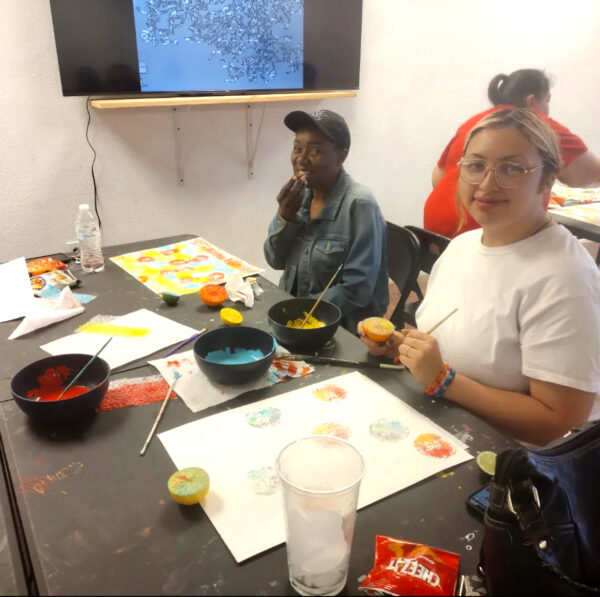 A photograph of two people seated at a table and painting.