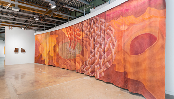 Installation image of a large scale fabric piece suspended from the ceiling and two small works on the wall