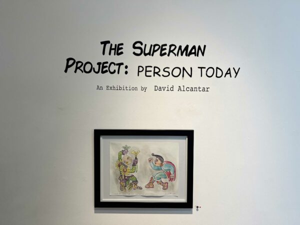 Exhibition title wall with a small framed drawing of superman fighting an aztec warrior
