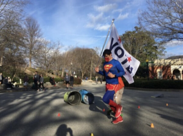 David Alcantar dressed as superman running with a VOTE flag