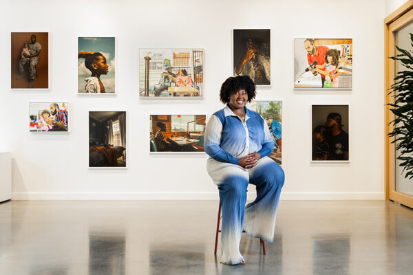 A photograph of Jakayla Monay sitting in front of a wall of photographs and paintings.