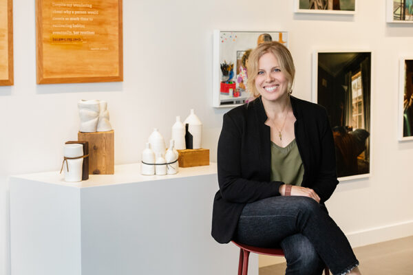 A photograph of artist Jessica Phillips sitting in front of small sculptures on table.