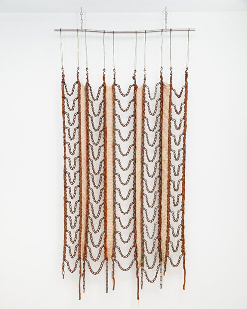 A photograph of a hanging textile piece by Kaleta Doolin, made from chains, wool, and yarn.