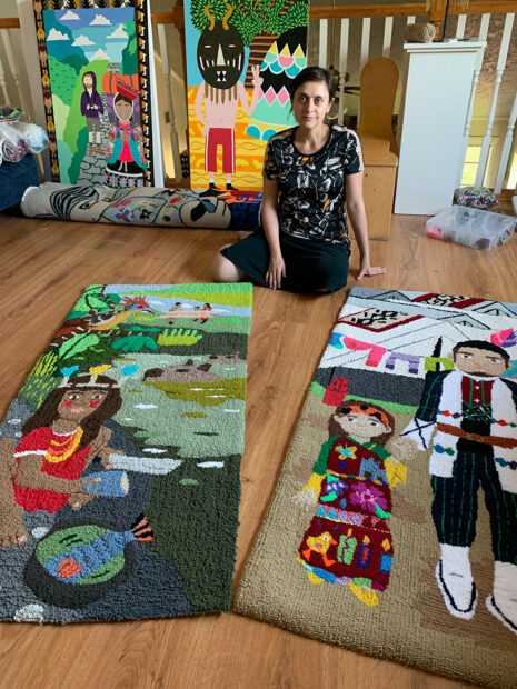 A photograph of artist Nela Garzón in her studio with paintings and tufted rug pieces.