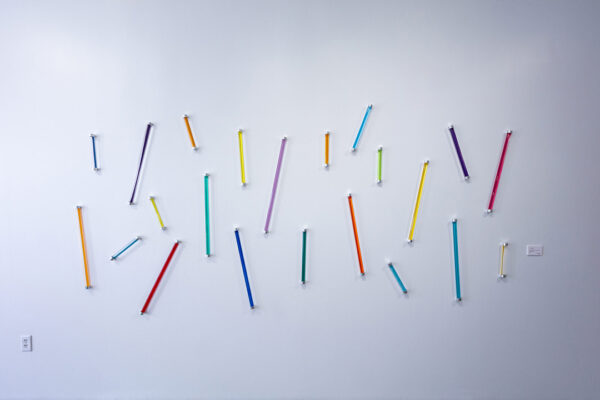An installation image of a work by Lorena Morales including an array of colorful tubes attached to a wall.