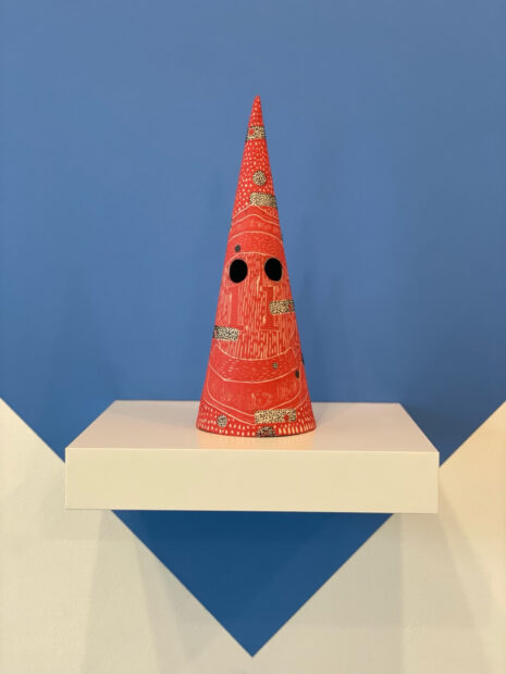 Orange cone shaped ceramic sculpture on a white pedestal with a blue background