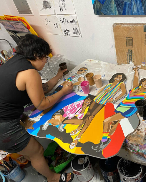 A photograph of artist Suzy Gonzalez working on a painting in her studio.