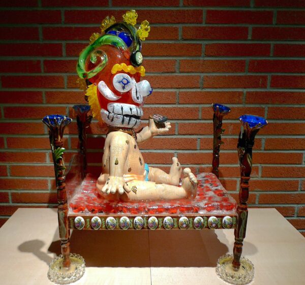 Sculpture of a baby in a bed wearing an aztec mask