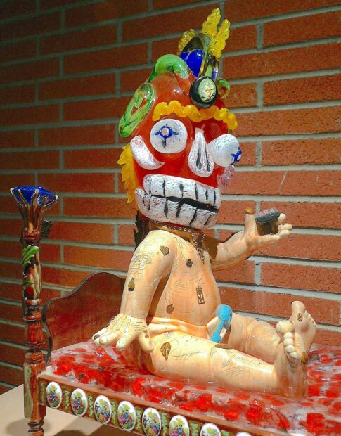 Sculpture of a baby in a bed wearing an aztec mask