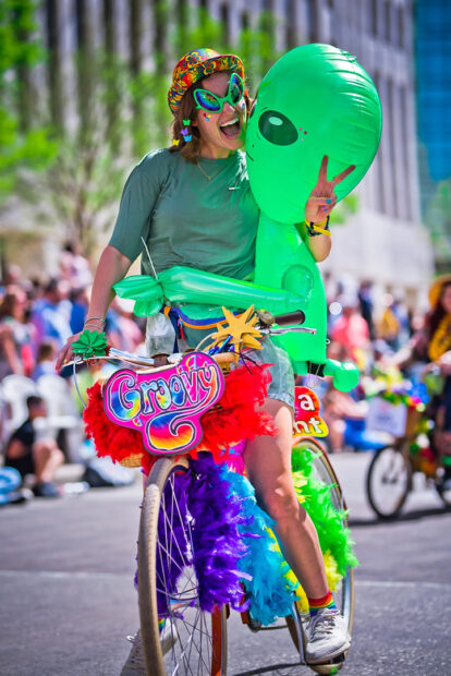 A photograph of a woman riding a decorated bicycle in a parade.