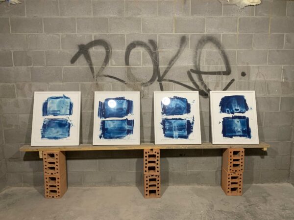 Four framed artworks sit on a piece of wood, which is propped up using bricks.