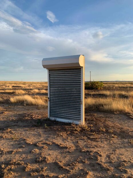 A large roll gate, used for securing storefronts, sits in a West Texas desert landscape.