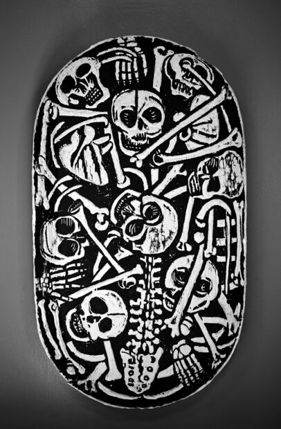 An overhead photograph of a large wooden bowl with skeleton figures carved into it. Artwork by Eric Avery.