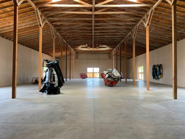 Multiple sculptures of crumpled car parts sit in a large warehouse building.