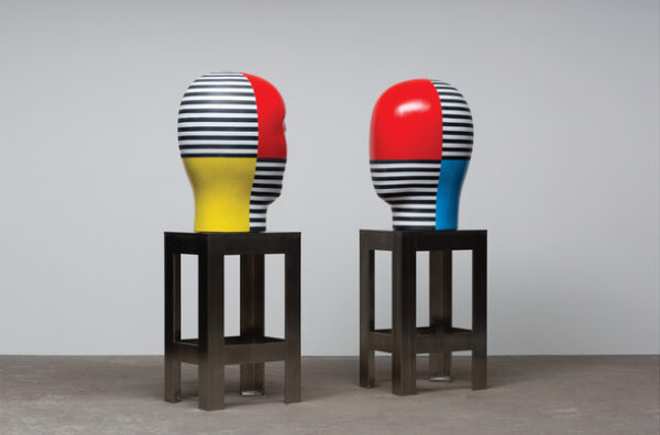 A photograph of two large ceramic statues of abstract heads sitting on stainless steel bases.