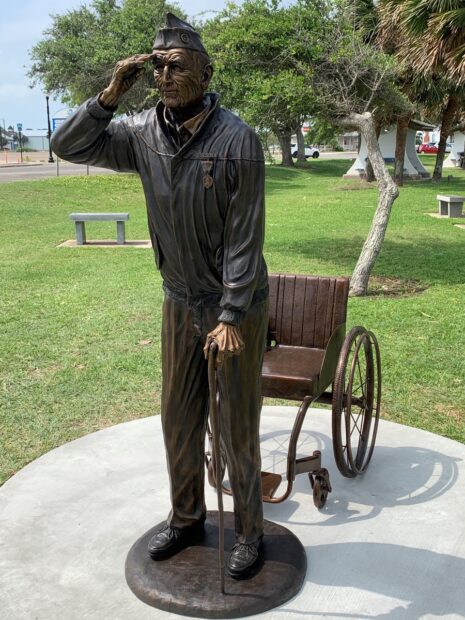 A photograph of a sculpture of an elderly veteran standing in front of his wheelchair and saluting as he looks into the distance.