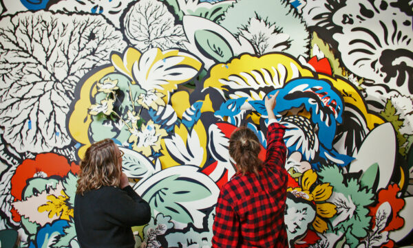 Two women standing in front of a large painted mural