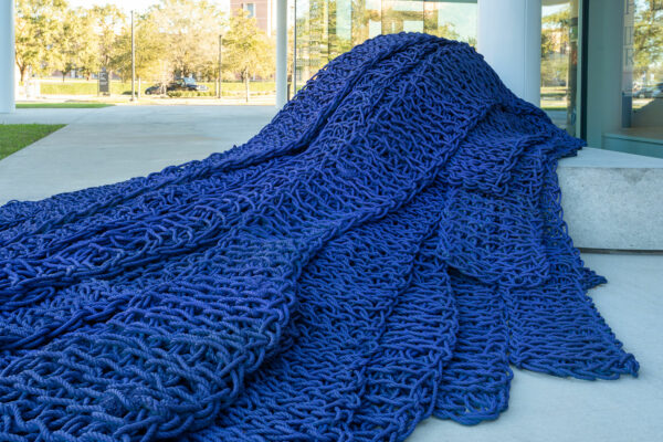 Installation view of a large knitted blue rope piece cascading from the stairs of the Moody Center for the Arts