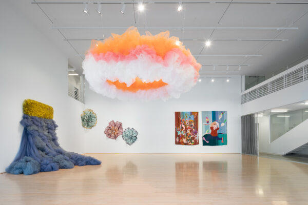 Installation view on Narrative Threads with a large fabric piece cascading from the wall and an orange, white, and pink tulle cloud hanging from the ceiling