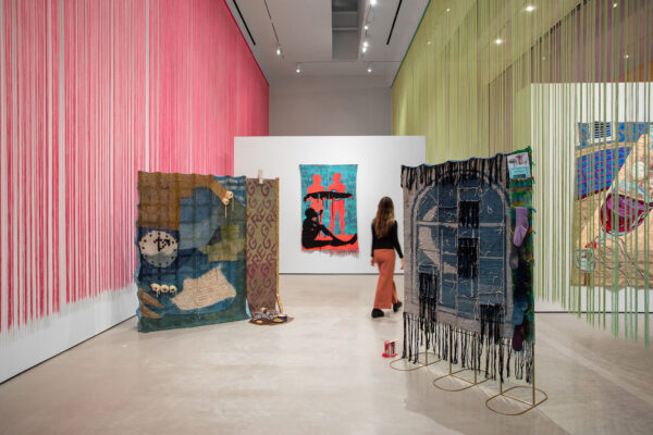 Installation view of Narrative Threads with hanging fabric pieces in strings, and tapestries suspended from armatures