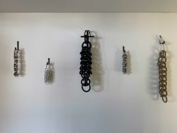 Chain-looking artworks, made of various fired ceramic materials, hang on a wall.